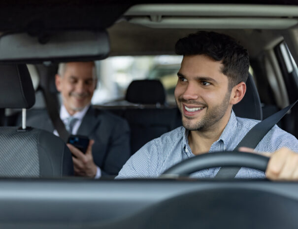 Happy Latin American driver transporting a business man on a crowdsourced taxi - transportation concepts