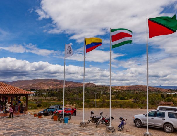 Moniquirá, Colombia - September 14, 2014: Moniquirá near the town of Villa de Leyva; it is home to the Museo El Fósil and several handicraft shops. It is popular with both Colombian and international tourists.  The Museo or Meuseum, has been constructed over the 110 Million year old Kronosaurus Boyacensis fosil found by a local peasant in 1977. The area was covered by shallow inland seas in the Cretaceous period. Photo shows flags and a handicraft shop near the entrance. The flags represent the Museum, Colombia, the Department of Boyaca and the town of Villa de Leyva. Visitors vehicles are parked in front and in the far background are the always present Andes Mountains: the Corsillera Oriental.  Photo shot in the morning sunlight; horizontal format. Copy space. Camera: Canon EOS 5D MII. Lens Canon EF 24-70mm F2.8L USM.